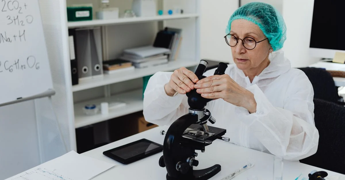 Scientifique féminine âgée en EPI examinant des échantillons avec un microscope dans un laboratoire moderne.