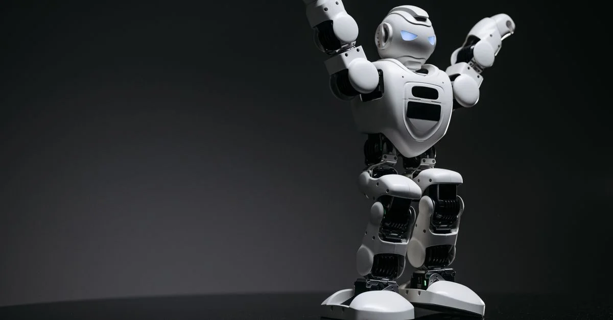 Gros plan en studio d'un jouet robot blanc avec des yeux LED levés en signe de victoire sur un fond gris.